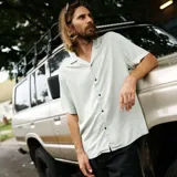 Camisa de manga corta color verde claro, con cuello tipo cubano y cierre frontal con botones marrones.