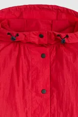 Campera parka roja estilo blouson con capucha ajustable, cierre frontal de botones a presión, bolsillos frontales con solapa y diseño holgado.