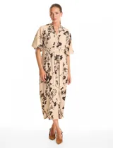 Vestido maxi de crepe color beige con estampado floral en tonos marrones y negros. Presenta cuello a la base, escote en V, abertura central con botones y cintura con lazo de ajuste y hebilla.