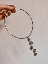 Gargantilla rígida plateada con dije colgante de alpaca con cinco piezas circulares irregulares.