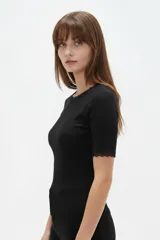 Remera de algodón negro con textura acanalada, manga corta y cuello redondo base. Presenta sutiles detalles de puntilla en el cuello y en los bordes de las mangas.