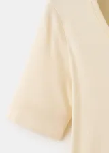 Camiseta de punto de algodón en color beige claro, con cuello redondo y mangas cortas. Diseño ajustado y estilo minimalista.