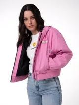 Chaqueta de lona color rosado con capucha ajustable, cierre frontal con cremallera y forro interior acolchado con diseño de diamantes. Presenta puños y bajo acanalados, bolsillos laterales y parche con el logo de la marca en el pecho.