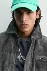 Cazadora de corte relajado confeccionada en piel con acabado de serraje. Presenta cuello solapa, cierre frontal con cremallera oculta bajo solapa con botones a presión, bolsillo con cremallera en el pecho y bolsillos de plastrón con solapa en la cadera. Incluye efecto vintage en las costuras y puños con botón.