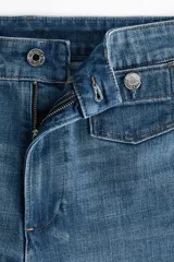 Jean tobillero de denim azul con leve stretch, tiro alto y piernas amplias de corte ancho. Presenta bolsillos de parche delanteros con botón y pliegues marcados.