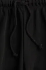 Pantalón tipo jogger de felpa color negro, con cintura elástica ajustable mediante cordón. Presenta un corte amplio y recto en las piernas, con bolsillos laterales discretos.