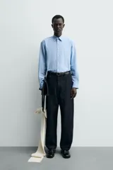 Camisa de algodón celeste con rayas verticales finas en blanco, de corte relajado (relaxed fit), cuello solapa y manga larga con puño abotonado.