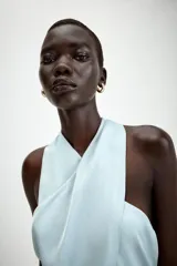 Top de cuello halter con diseño cruzado en el frente, confeccionado en tejido satinado. Presenta bajo asimétrico con detalle de lazada y cierre posterior con botones.