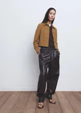 Chaqueta de ante color marrón claro, de diseño corto y recto, con cuello camisero, manga larga, dos bolsillos de parche delanteros y cierre frontal con botones.