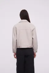 Chaqueta corta color arena melange con cuello camisero, cierre frontal con botones dorados y bolsillos de parche en el pecho.