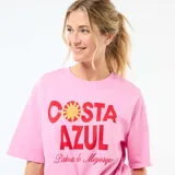 Camiseta de corte oversize color rosa, con cuello redondo y mangas cortas. Presenta un estampado frontal con la frase 'COSTA AZUL' en letras rojas y un diseño de sol, acompañado por la inscripción 'Palma de Majorque'.
