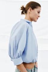 Camisa de algodón con cuello solapa, mangas abullonadas por debajo del codo y bajo acabado en globo. Presenta cierre frontal con botones ocultos.
