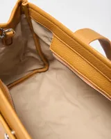 Cartera tipo tote XL confeccionada en símil cuero de textura granulada color habano. Cuenta con doble asa de mano, detalles de correas decorativas con hebilla en los laterales y un charm colgante en forma de corazón. Incluye placa metálica con las iniciales de la marca en el frente.