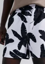 Short de baño blanco con estampado de hojas negras, cintura elástica y bolsillos laterales.