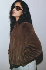 Campera de textura suave efecto peluche, color marrón, con cuello redondo, cierre frontal con botones y forro interior.