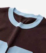 Remera marrón de manga corta con cuello redondo y ribetes celestes en cuello y puños. Presenta un gran estampado numérico "86" en color celeste en el pecho.