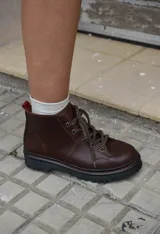 Borcegos de cuero charolado negro con cordones jaspeados en tonos marrones y suela track dentada con costura blanca visible.