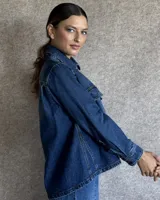 Sobrecamisa de denim azul con cuello camisero, cierre frontal con botones, mangas largas con puños abotonados y dos bolsillos con solapa en el pecho.