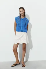 Chaleco azul de punto calado con cuello redondo, sin mangas, cierre frontal con botones y dos bolsillos de parche en la parte delantera.