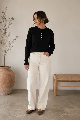 Sweater de punto negro en doble hilado Bremer, con cuello redondo y cierre frontal parcial de botones blancos con ribetes ondulados, mangas largas con puños elastizados y volados sutiles en el cuello y los puños.