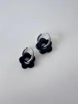 Aros de acero quirúrgico plateado tipo argolla con un dije colgante en forma de flor de color negro.