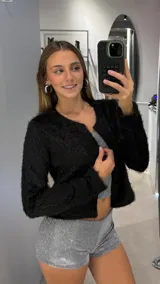 Chaqueta corta de textura peluda en color negro, con cuello redondo y cierre frontal abierto. Presenta mangas largas y un corte recto.