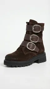 Bota de caña media en gamuza negra, con suela track dentada y tres correas horizontales con hebillas metálicas plateadas.