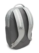 Mochila Under Armour modelo Hustle 6.0, color gris, con tecnología UA Storm resistente al agua. Cuenta con compartimento acolchado para portátil, bolsillo para calzado o ropa sucia, bolsillos laterales de malla y sistema Molle para sujeción.
