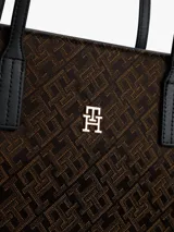Cartera tipo tote de Tommy Hilfiger con diseño jacquard de monogramas TH en color marrón y laterales en negro. Cuenta con asas superiores fijas y logo metálico dorado en el frente.