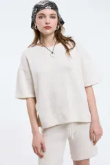 Top tejido de punto color crudo, con cuello a la base y mangas cortas holgadas. Presenta un diseño minimalista y relajado.