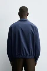 Cazadora regular fit color beige, confeccionada en tejido de algodón. Cuenta con cuello solapa, manga larga con puño elástico y trabilla, bolsillos de vivo en la cadera, bajo elástico y cierre frontal con cremallera.