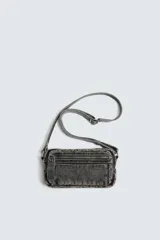 Bandolera de tejido denim con efecto lavado, cuenta con compartimento principal con cierre de cremallera, bolsillo interior con cierre y asa de hombro ajustable.