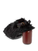 Sueco negro con pelo sintético, taco de madera y hebilla trasera para ajustar al talón.