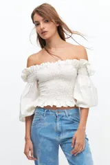 Crop top blanco con escote off-shoulder, punto panal en el torso y volados en el escote.