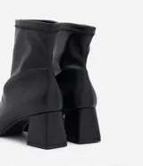 Bota de caña corta color negro, confeccionada en material sintético, con taco mediano bloque y puntera cuadrada.