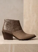 Bota corta de cuero vacuno con diseño de texturas combinadas: cuero con grabado tipo cocodrilo en el talón, gamuza en el lateral y cuero texturizado en la puntera. Presenta un taco cuadrado de madera de 6 cm y punta fina.