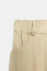 Falda midi de tiro alto color beige, con bolsillos delanteros, cintura con trabillas y cierre frontal con cremallera y ganchos metálicos.