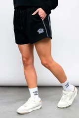 Short deportivo Umbro para mujer de color negro, con bolsillos laterales, cordón ajustable en la cintura y ribete blanco en los laterales. Presenta el logo de la marca bordado en la pierna.
