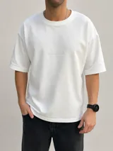 Remera oversize de algodón color off white, de corte holgado y manga corta, con cuello redondo y pequeño texto bordado en el centro del pecho.