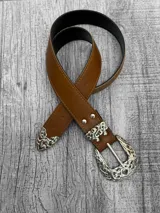 Cinto de cuero color marrón con hebilla metálica plateada con diseño labrado.