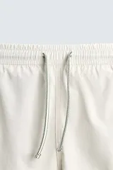 Bañador de hombre color blanco con diseño de bandas verticales en tonos de verde, simulando un efecto tie-dye o acuarela. Posee cintura ajustable con cordón, bolsillos laterales y forro interior.