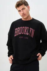 Buzo negro de corte holgado con estampa frontal de letras en color borgoña que dice "BROOKLYN" y "NEW YORK".
