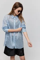Camisa de rayas de calce relajado, confeccionada en tejido liviano y semitransparente, con cuello clásico, cierre frontal con botones, mangas largas con puños y hombros caídos.