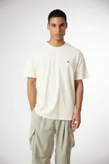 Remera de algodón de corte holgado, color blanco crema, con cuello redondo y pequeño parche bordado en el pecho.