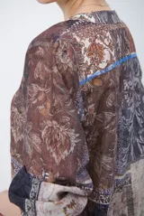 Camisa de corte recto con cuello mao y cierre frontal parcial de botones. Presenta un diseño estampado tipo patchwork con motivos florales y geométricos en tonos tierra, marrones y beige. Posee mangas tres cuartos con puños simples.