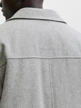 Campera bomber corta de paño gris claro, con cuello camisero, cierre frontal metálico completo y bolsillos laterales ribeteados. Presenta puños y cintura elasticados en rib acanalado.