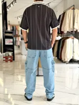 Camiseta deportiva blanca de manga corta con rayas verticales negras, cuello polo en V de color negro con ribete blanco, y puños negros. Cuenta con estampado frontal con la palabra "TOKIO" en grande, además de detalles gráficos y texto en el pecho.