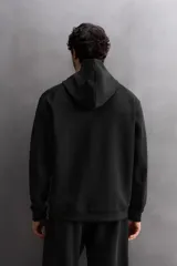 Sudadera con capucha y cierre de cremallera frontal, color negro, confeccionada en tejido técnico compacto de algodón elástico. Presenta cuello subido, bolsillos frontales con cremallera y acabado termofijado, y puños y bajo en rib del mismo tejido.