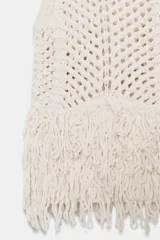 Chaleco de punto calado color crudo, de cuello redondo y sin mangas. El bajo está terminado con flecos.