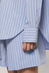 Camisa Sailor Line de calce holgado y diseño a rayas. Presenta cuello camisero, mangas largas y puños abotonados. Cuenta con acceso frontal mediante botones a tono y detalle bordado en el pecho.